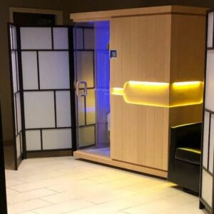 Infrared sauna cabin glowing with yellow and blue light behind folding screens in the Thrive sauna lounge
