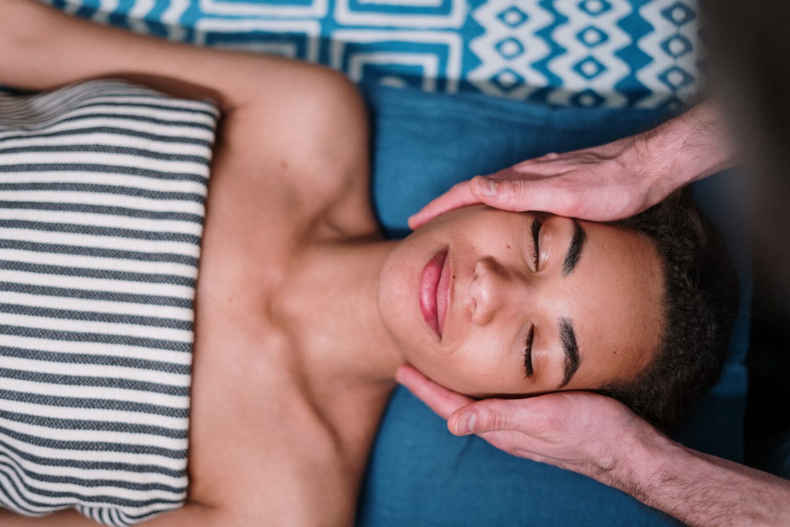 Overhead view of a woman with closed eyes and a relaxed smile as a therapist's hands cradle her face