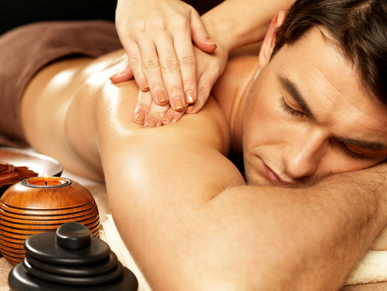 Man resting face down during a shoulder massage, a lit candle beside him