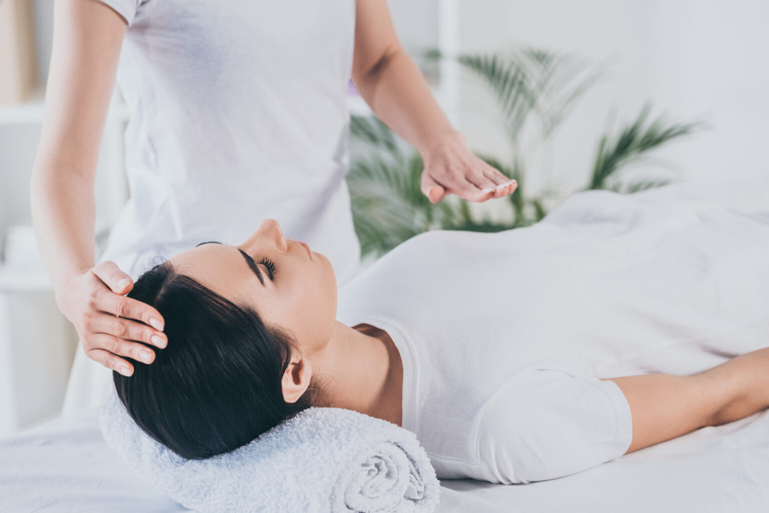 Woman lying on a table with her eyes closed while a Reiki practitioner holds their hands above her forehead