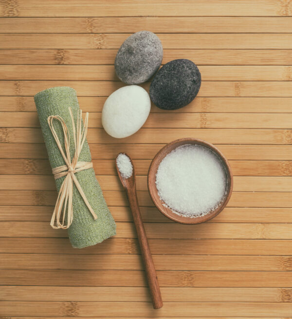 Massage stones, a rolled towel and a bowl of scrub on a wooden spa table