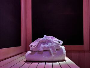 Folded spa robe resting on a folded towel on a sauna bench in soft pink light