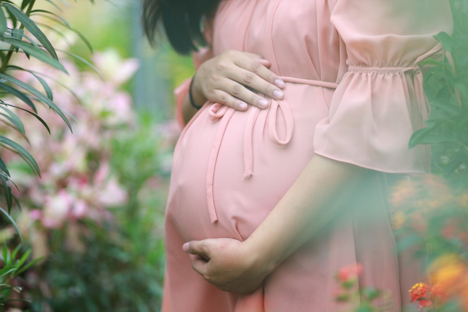 Pregnant woman in a pink dress cradling her belly in a flowering garden