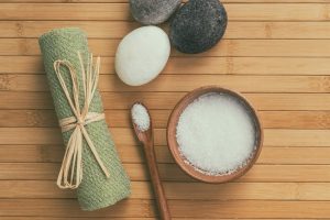 Bath salts natural spa products top view on bamboo wooden texture background with copy space for wellness health concepts. Hot stone massage and exfoliation towel salt in wood bowl.